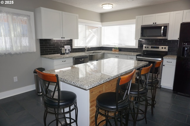 kitchen with stainless steel appliances, white cabinetry, a sink, and a kitchen breakfast bar