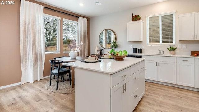 kitchen featuring white cabinets, a center island, sink, and light wood-type flooring