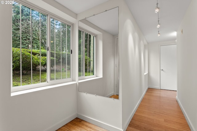 hallway featuring rail lighting, baseboards, and light wood-style floors