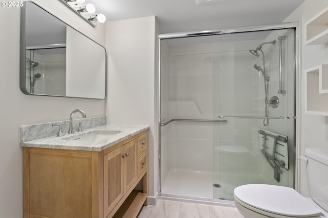 bathroom with vanity, toilet, wood finished floors, and a stall shower