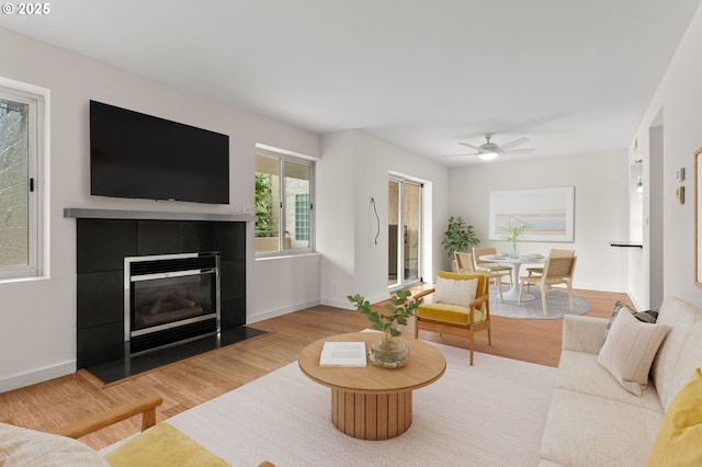 living room featuring ceiling fan, wood finished floors, baseboards, and a tile fireplace