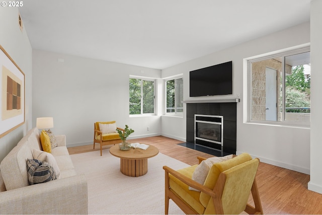 living area with a healthy amount of sunlight, wood finished floors, and a tile fireplace