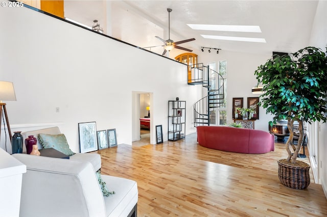 living area with a skylight, ceiling fan, wood finished floors, high vaulted ceiling, and stairs