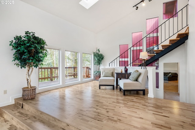 sitting room with high vaulted ceiling, a skylight, wood finished floors, stairs, and rail lighting