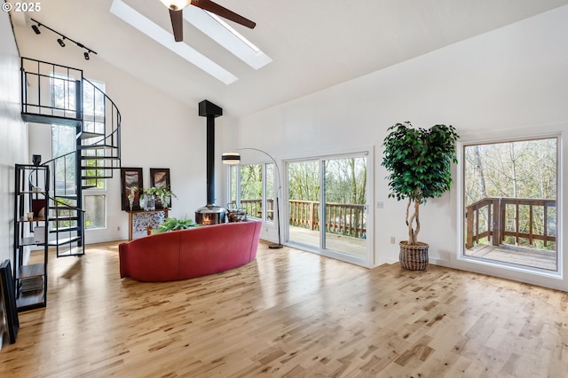 living room featuring stairway, a wood stove, a healthy amount of sunlight, wood finished floors, and high vaulted ceiling