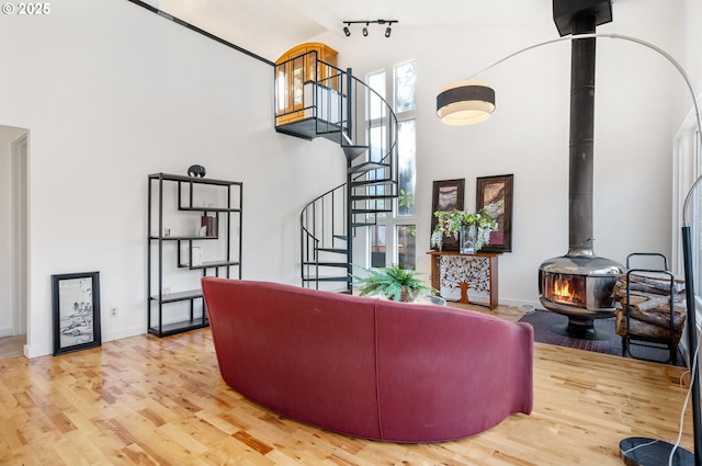 living area with high vaulted ceiling, stairway, wood finished floors, and a wood stove