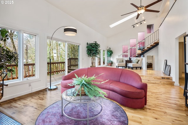 living area with high vaulted ceiling, a skylight, wood finished floors, a ceiling fan, and stairway