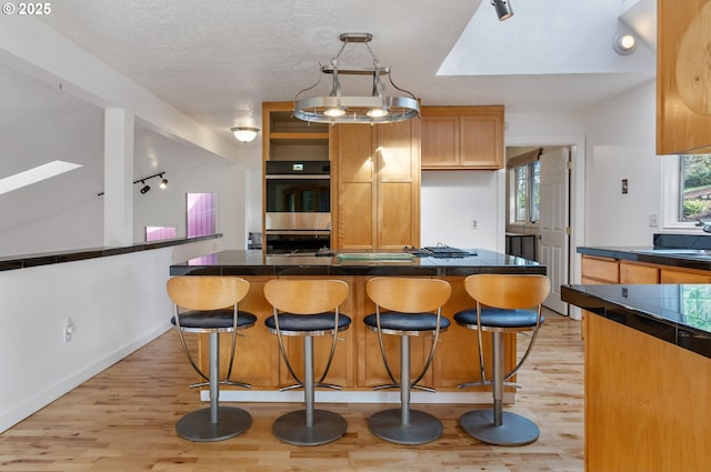 kitchen with dark countertops, light wood-style floors, a kitchen bar, and stainless steel double oven