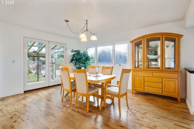 dining room featuring light wood-type flooring, baseboards, a notable chandelier, and french doors