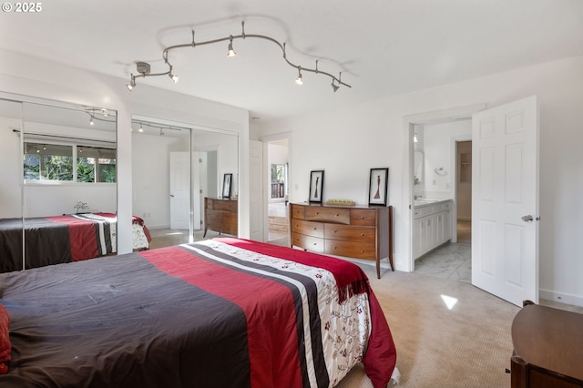 bedroom featuring baseboards, ensuite bathroom, track lighting, and light colored carpet