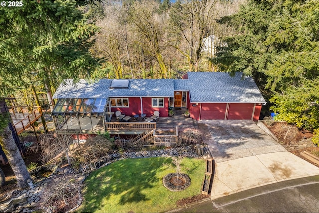 view of front of home featuring an attached garage, a shingled roof, driveway, a wooden deck, and a front lawn