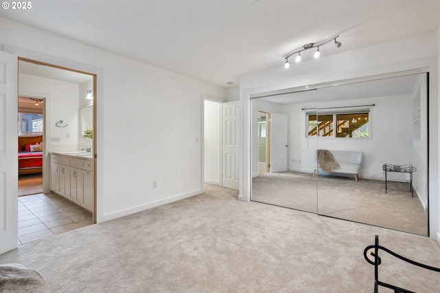 unfurnished bedroom featuring a closet, light colored carpet, a sink, and baseboards