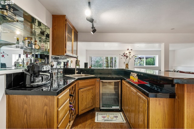 kitchen with beverage cooler, wood finished floors, a sink, brown cabinetry, and glass insert cabinets