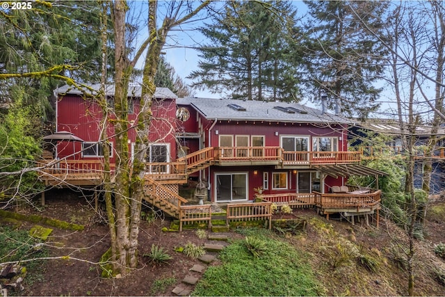 rear view of house with a wooden deck, stairway, a barn, and roof with shingles