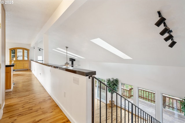 hall with lofted ceiling with skylight, a wealth of natural light, light wood-style floors, and an upstairs landing