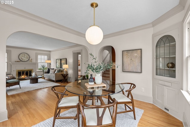 2815 NE 35th Ave, Portland, OR 97212 - dining room with crown molding, light wood-style floors, arched walkways, baseboards, and a glass covered fireplace