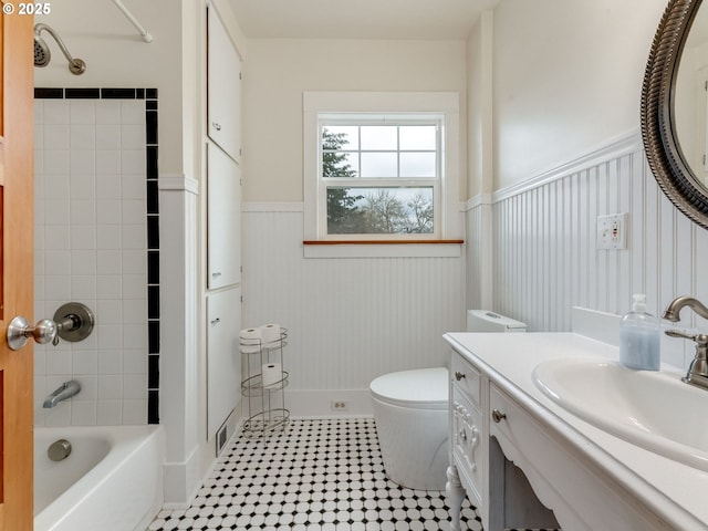 bathroom with a wainscoted wall, shower / washtub combination, toilet, and vanity