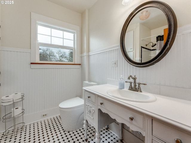 bathroom featuring vanity, toilet, and a wainscoted wall