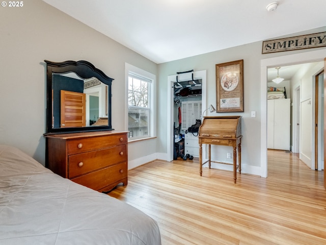 bedroom featuring a spacious closet, light wood-style flooring, a closet, and baseboards