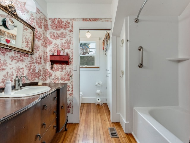 full bathroom featuring baseboards, visible vents, wallpapered walls, hardwood / wood-style flooring, and toilet