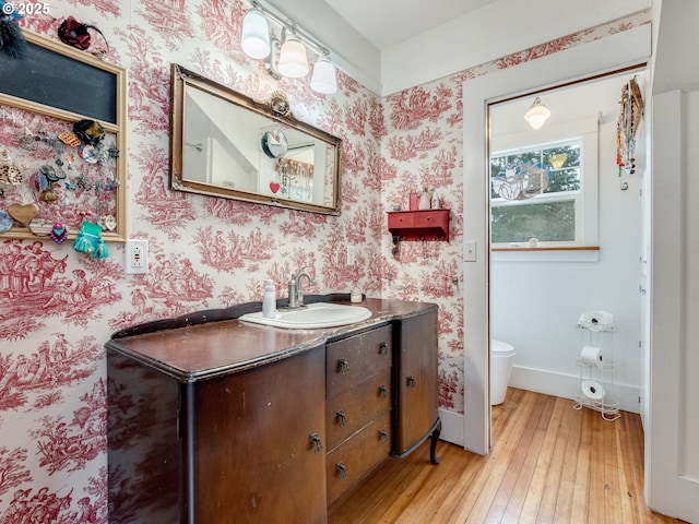 bathroom featuring toilet, hardwood / wood-style flooring, wallpapered walls, baseboards, and vanity