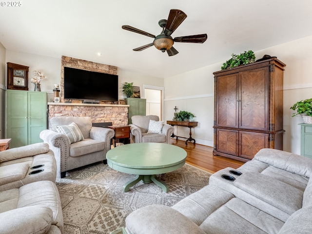 living area featuring baseboards, a fireplace, a ceiling fan, and light wood-style floors