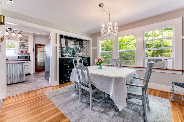 dining space with cooling unit, light wood-style floors, baseboards, and a chandelier