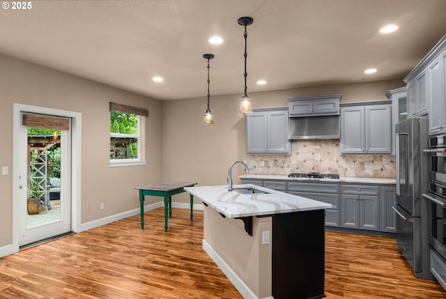 kitchen with tasteful backsplash, wood finished floors, a sink, gray cabinetry, and recessed lighting