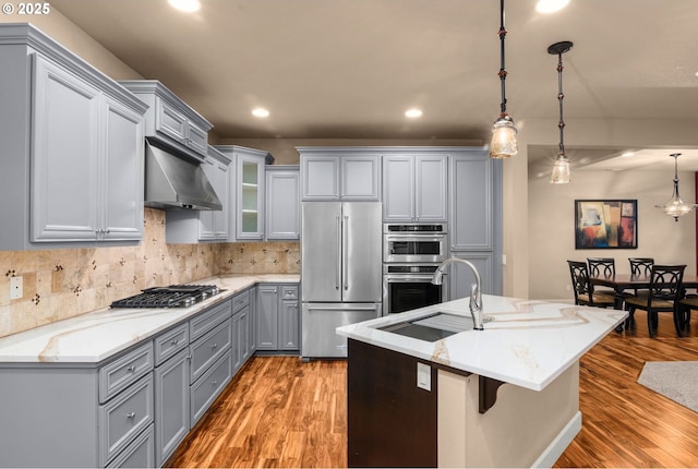 kitchen with appliances with stainless steel finishes, light wood-style floors, decorative light fixtures, backsplash, and gray cabinetry