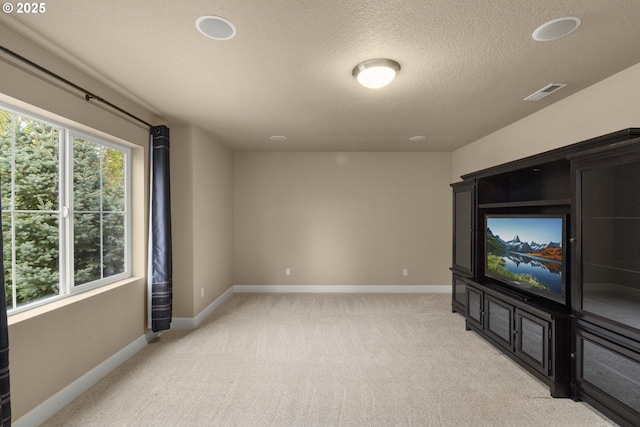 unfurnished living room with a textured ceiling, baseboards, light colored carpet, and visible vents