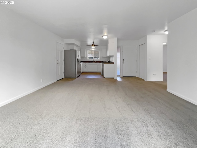 unfurnished living room with a sink, baseboards, and light carpet