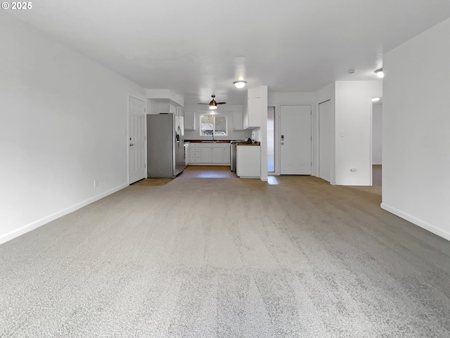 unfurnished living room featuring a sink, baseboards, and light colored carpet