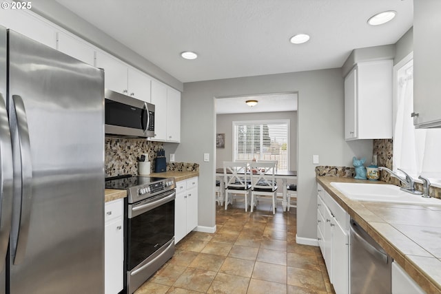 kitchen with sink, appliances with stainless steel finishes, tasteful backsplash, tile counters, and white cabinets