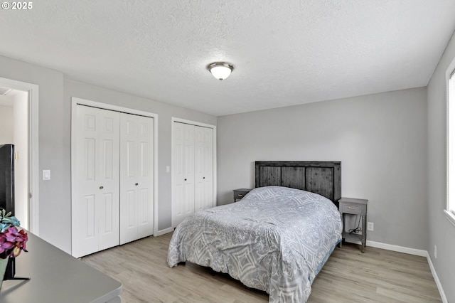 bedroom featuring light wood-type flooring, a textured ceiling, and two closets