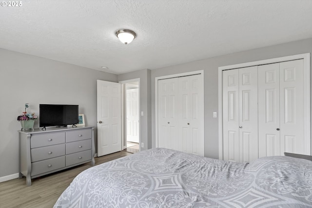 bedroom featuring multiple closets, a textured ceiling, and light wood-type flooring