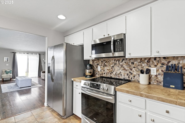 kitchen with light tile patterned floors, appliances with stainless steel finishes, tasteful backsplash, a textured ceiling, and white cabinets