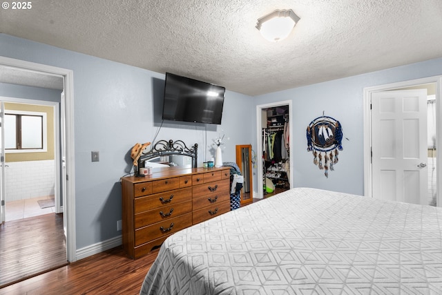 bedroom with a textured ceiling, a walk in closet, a closet, and dark hardwood / wood-style floors