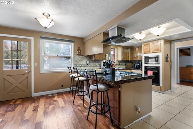 kitchen featuring kitchen peninsula, light hardwood / wood-style flooring, stainless steel appliances, decorative backsplash, and a kitchen breakfast bar