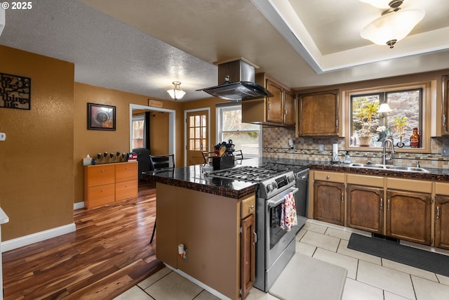 kitchen with stainless steel gas stove, kitchen peninsula, ventilation hood, light tile patterned floors, and sink