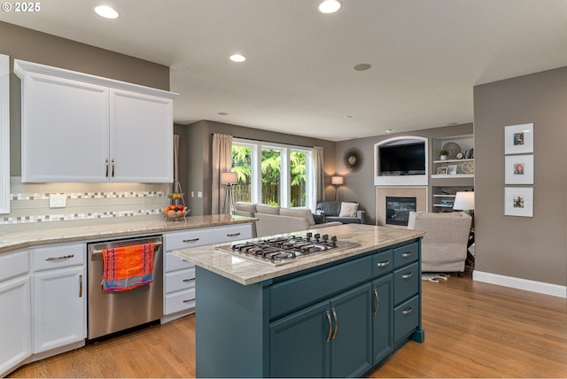 352 SE 14th Pl, Canby, OR 97013 - kitchen with stainless steel appliances, white cabinets, light wood-style flooring, a tiled fireplace, and backsplash