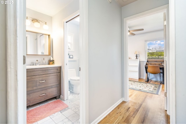 bathroom with baseboards, a ceiling fan, toilet, wood finished floors, and vanity