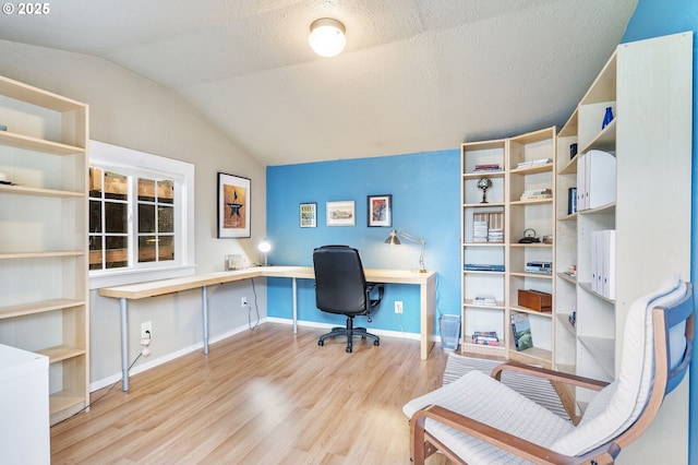 office space featuring light wood finished floors, built in study area, vaulted ceiling, a textured ceiling, and baseboards