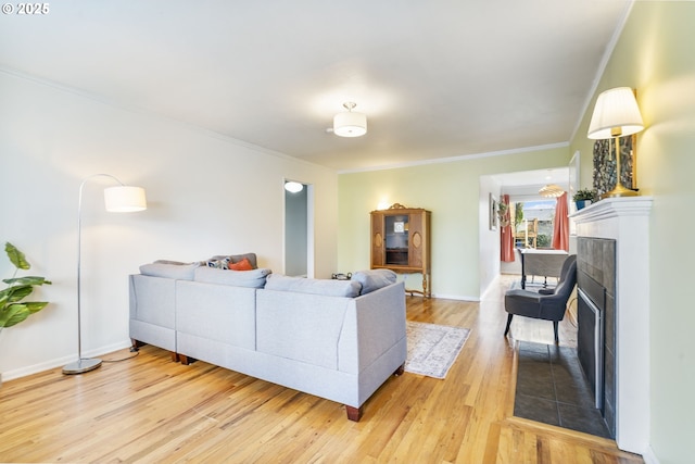 living area with a fireplace with flush hearth, ornamental molding, baseboards, and wood finished floors