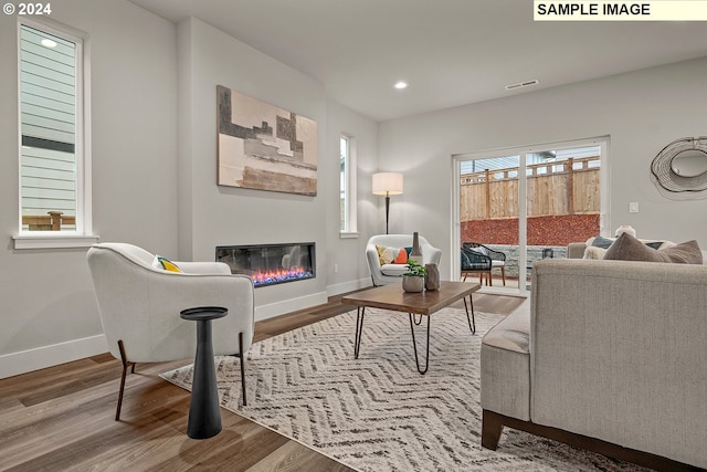 living room featuring a glass covered fireplace, recessed lighting, baseboards, and wood finished floors