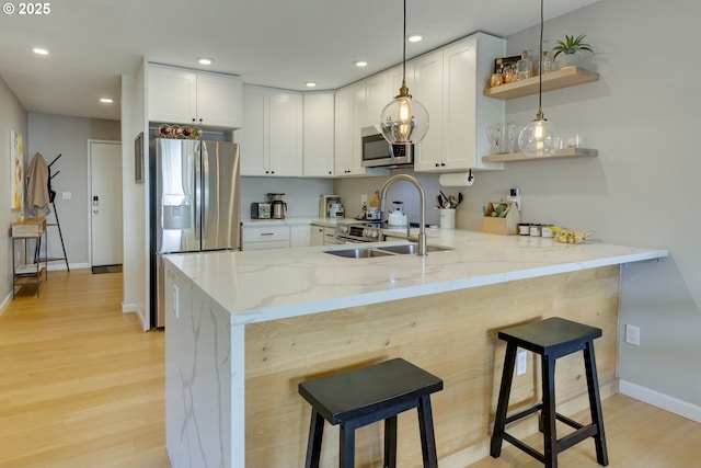 6825 SW Capitol Hill Rd Unit 27, Portland, OR 97219 - kitchen featuring a peninsula, stainless steel appliances, light stone counters, open shelves, and light wood finished floors