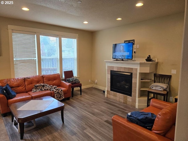living room featuring baseboards, recessed lighting, a tile fireplace, wood finished floors, and a textured ceiling