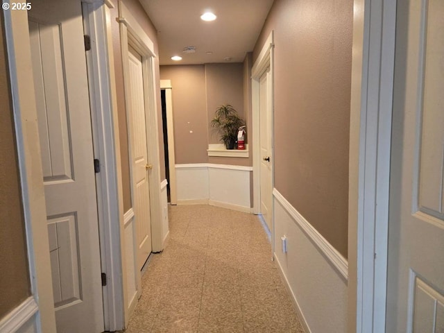hallway with wainscoting, a decorative wall, recessed lighting, and light floors