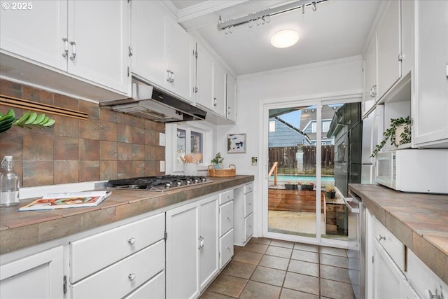 kitchen with white microwave, stainless steel gas cooktop, under cabinet range hood, white cabinetry, and backsplash