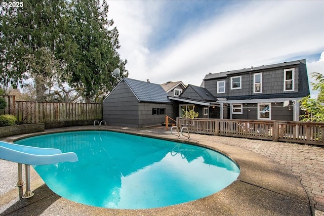 view of swimming pool with a patio, a fenced backyard, a water slide, a wooden deck, and a fenced in pool