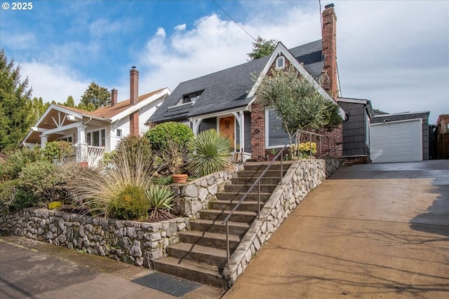 view of front of house with an outbuilding, covered porch, concrete driveway, a garage, and a chimney